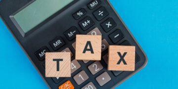 Tax planning concept with wooden cubes on calculator on blue background flat lay.
