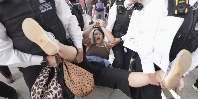 A woman is led away by police officers as supporters of Palestine Action take part in a mass action in Parliament Square, organised by Defend Our Juries as part of the Lift the Ban campaign, to end the proscription of Palestine Action, in London, Saturday, Aug. 9, 2025. (Stefan Rousseau/PA via AP)