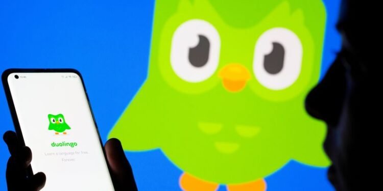 Woman with her smartphone poses in front of displayed Duolingo logo in this illustration taken, June 29, 2021. REUTERS/Dado Ruvic/Illustration