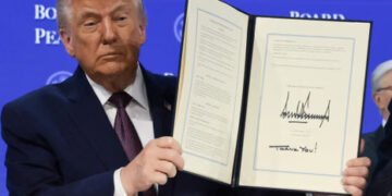 Trump unveils Davos Board of Peace, pitches $1B membership 11 Trump holds an open signed document in front of a blue backdrop reading “Board of Peace.”